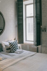 A cozy and stylish bedroom featuring modern decor and a sunlit window with shutter panels.